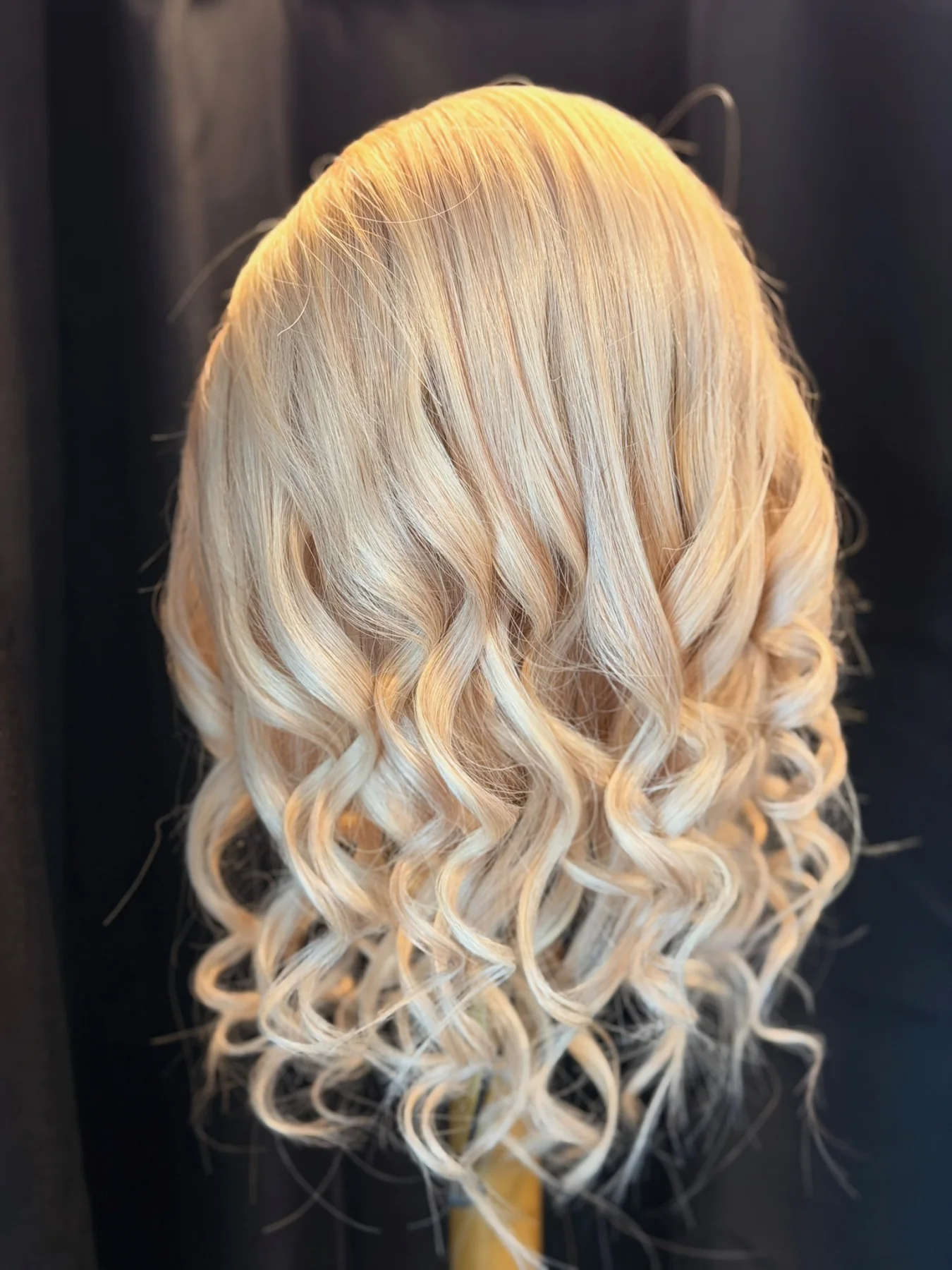 Platinum-blonde ponytail hairpiece with a smooth crown and loose spiral curls displayed against black