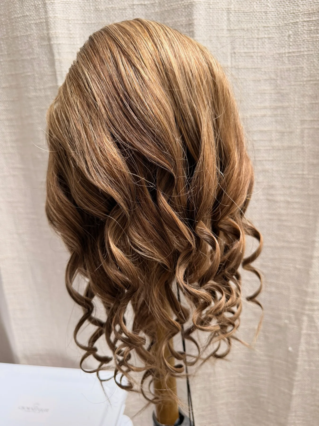 Warm caramel-brown highlighted ponytail hairpiece with loose spiral curls displayed on a stand