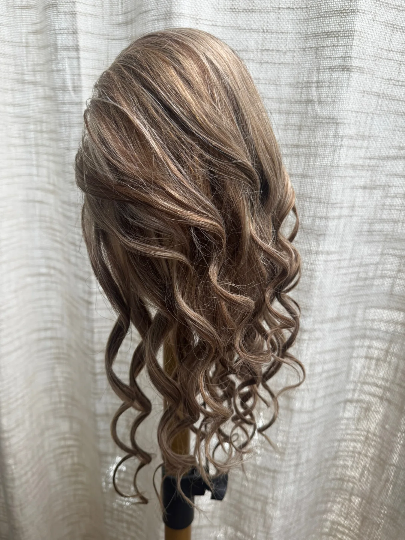 Ash-brown highlighted ponytail hairpiece with long ringlet curls displayed on a stand