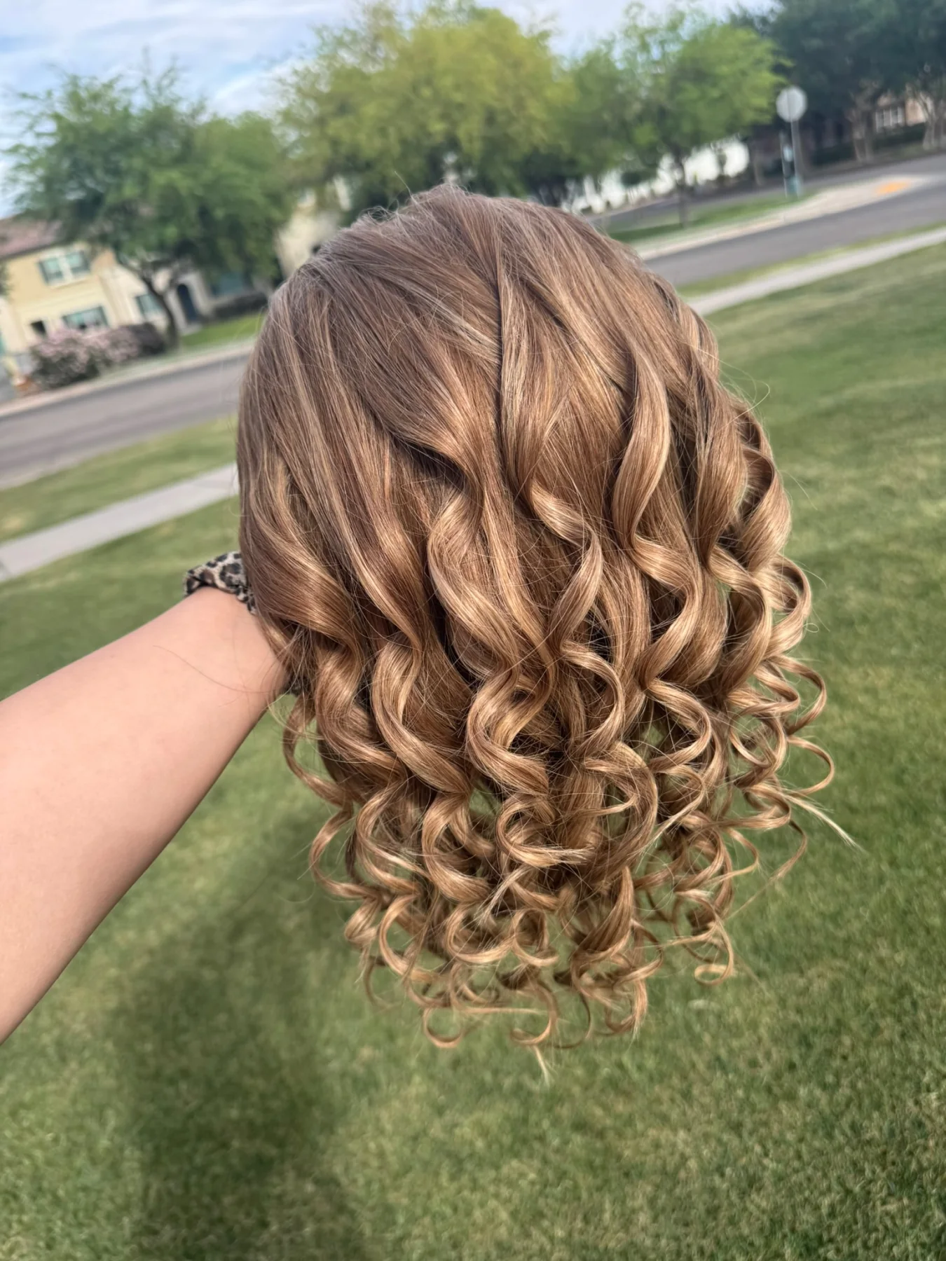 Warm brown highlighted ponytail hairpiece with defined spiral curls held outdoors