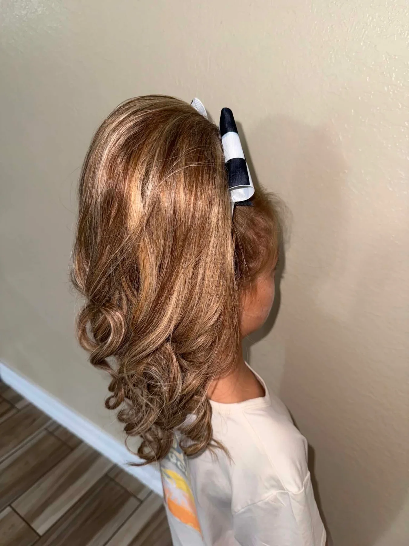 Side view of a young cheerleader wearing a caramel-brown curled ponytail with a black-and-white bow