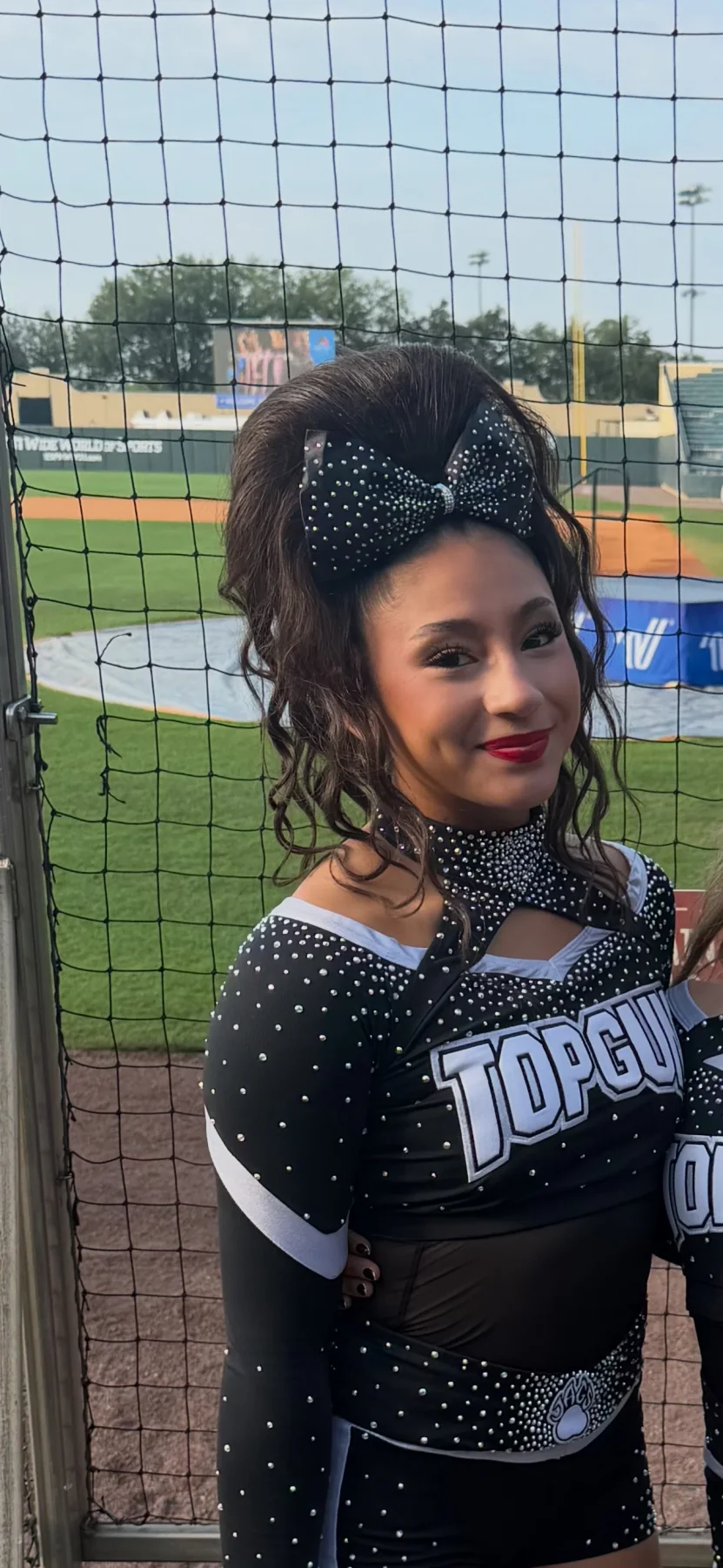Top Gun cheerleader at a ballpark wearing a dark curly ponytail and black rhinestone bow