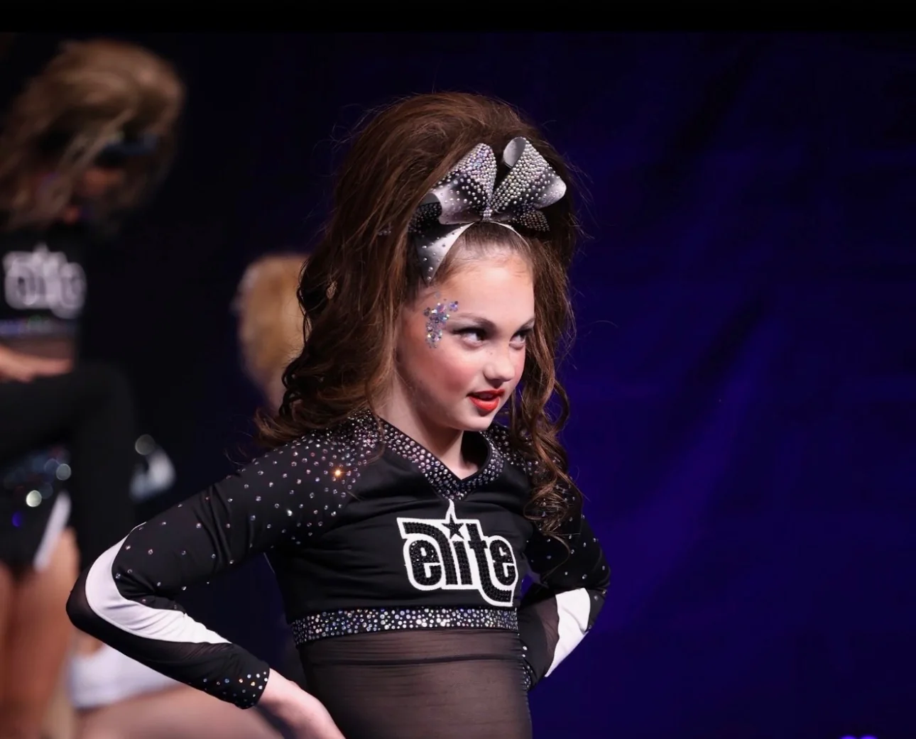 Elite cheerleader on stage wearing a curled brunette ponytail and silver-and-black rhinestone bow