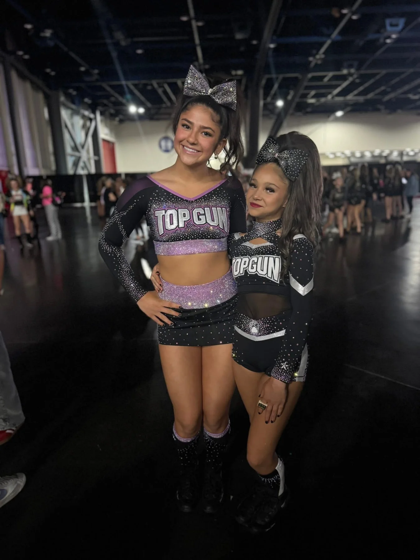 Two Top Gun cheerleaders at a competition wearing high ponytails and silver and black rhinestone bows